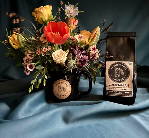 Floral arrangement in a Third Horse Coffee mug beside a bag of Guatemalan coffee, available from Kati Mac Floral Designs.