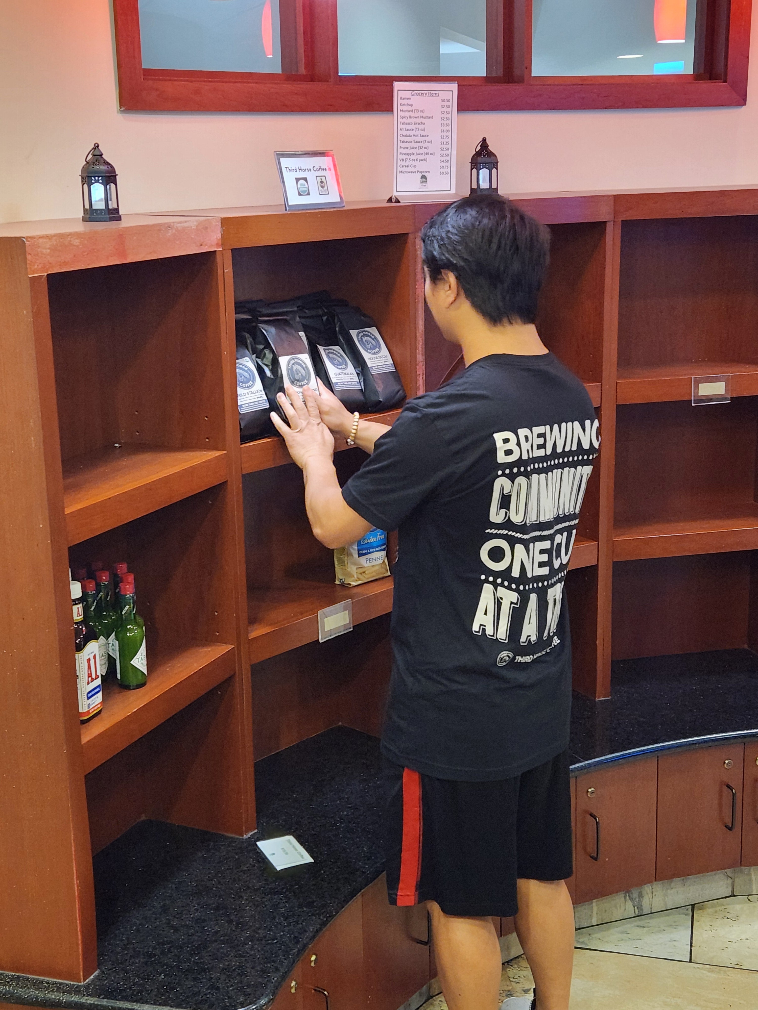 Josiah stocking Third Horse Coffee on the shelves at White Horse Village Market