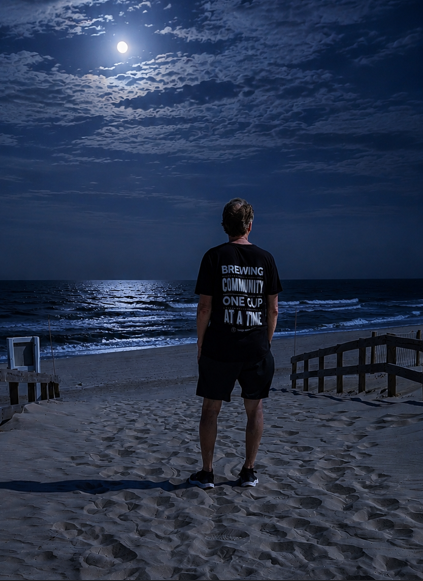 Third Horse Coffee co-founder wearing a “Brewing Community One Cup at a Time” shirt on the beach